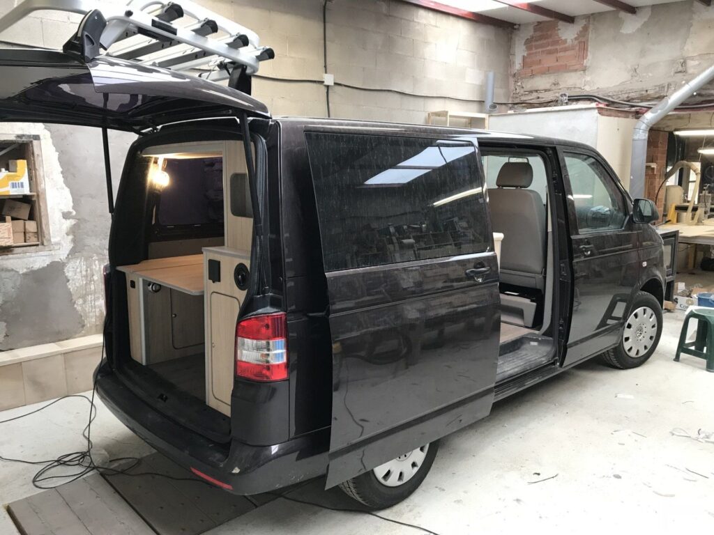 Detalle exterior de la Camper Volkswagen Transporter T5 convertida por Baovan, negro, puertas abiertas. Se aprecia la estructura de la cama y el almacenamiento debajo.