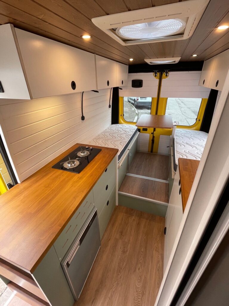 Espacio bien equipado dentro de la Peugeot Boxer L3H2 2+2 camper con área de comedor, cocina y acceso a la cabina.