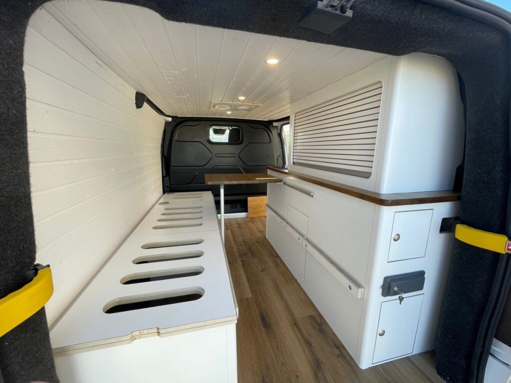 Interior de la furgoneta camper: blanco, suelo de madera, mucho espacio de almacenamiento