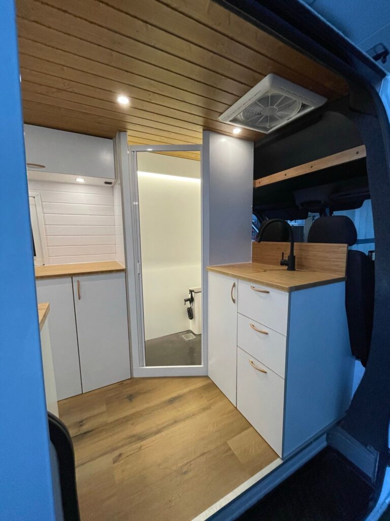 Mercedes Sprinter L4H2 Camper para 3 con Garaje con interior blanco y espacioso, cocina completa, armarios y baño completo.
