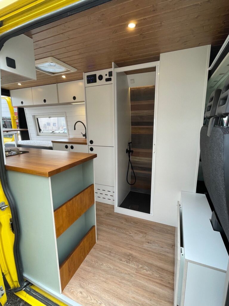 Vista interior de la Peugeot Boxer L3H2 2+2 camper con una cocina completa, incluyendo fregadero, estufa y espacios de almacenamiento.