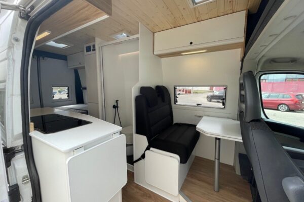 Vista lateral de la Citroën Jumper L4H3 4+4, convertida por Baovan Camper, mostrando toda la zona de descanso con la mesa plegable, los asientos y la cocina.