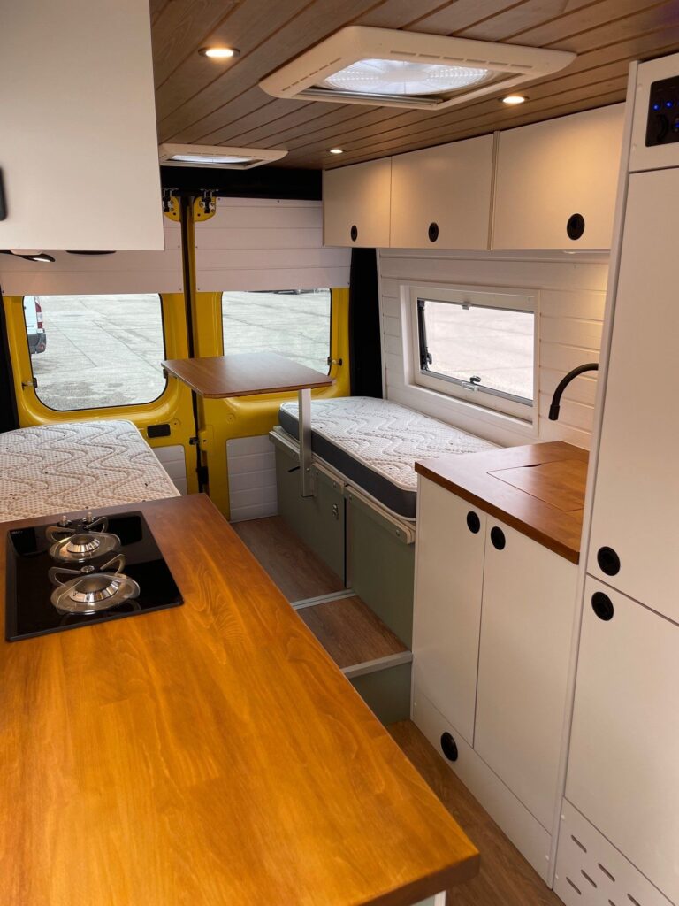 Área de descanso en la Peugeot Boxer L3H2 2+2 camper con cama doble y almacenamiento superior en un diseño compacto y funcional.