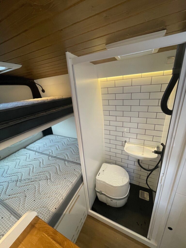 Detalle del baño completo con ducha de mano, lavabo y váter en la furgoneta Camper Peugeot Boxer L3H2 4+4.