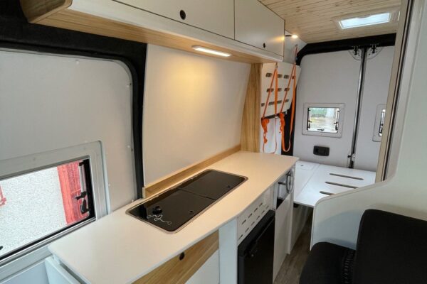 Detalle de la cocina, con fregadero, estufa, armarios, nevera y la cama al fondo en la Citroën Jumper L4H3 4+4, convertida por Baovan Camper.