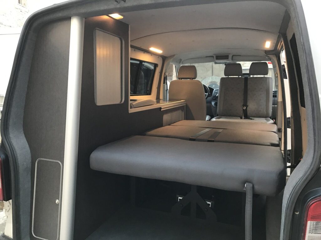 Detalles de la cama abierta en la furgoneta Camper VW Transporter T5 4Motion ocupando el espacio interno, junto a los armarios
