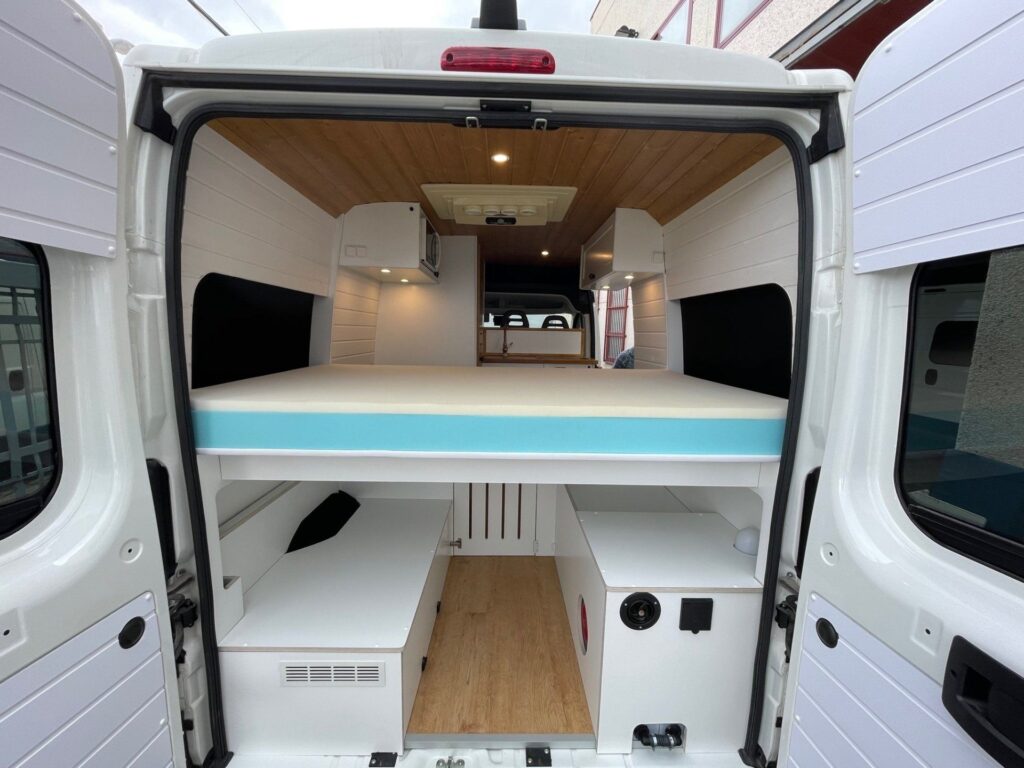 Detalhe visto de trás com porta traseira aberta, cama muito grande montada com espaço de armazenamento abaixo na furgoneta Boxer L2H2 3+3