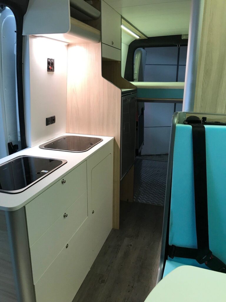 Vista interna de la cocina con armarios, fregadero y cocina en la Camper Peugeot Boxer L4H2 4+2