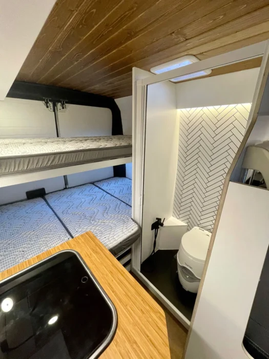 Detalle del área de descanso en la Peugeot Boxer Camper, con literas cómodas y acceso al baño compacto con decoración moderna.