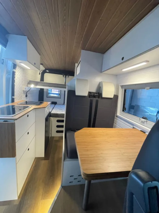 Vista del área de comedor y cocina en la Peugeot Boxer Camper, con mesa plegable y cocina integrada en un espacio optimizado.