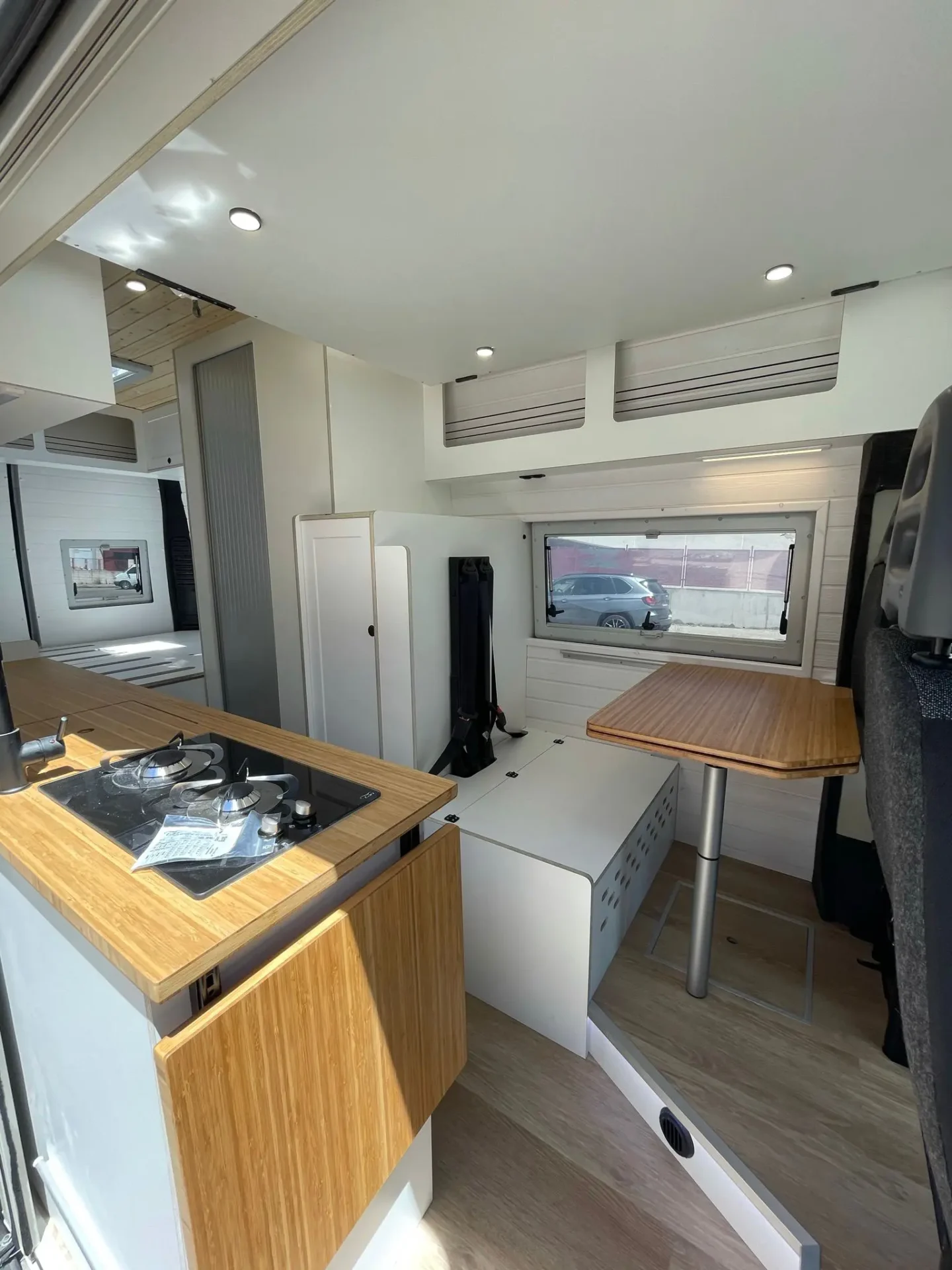 Espacio habitable multifuncional dentro de la furgoneta camper Ducato L4H3, con mesas plegables de madera, cocina integrada y áreas de almacenamiento optimizadas.