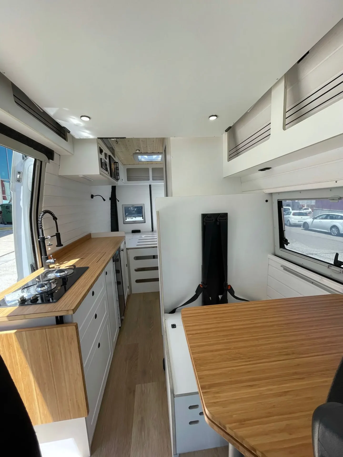 Vista del interior espacioso de una camperización personalizada de la furgoneta Ducato L4H3 mostrando una mesa de comedor de madera, cocina equipada y almacenamiento eficiente.