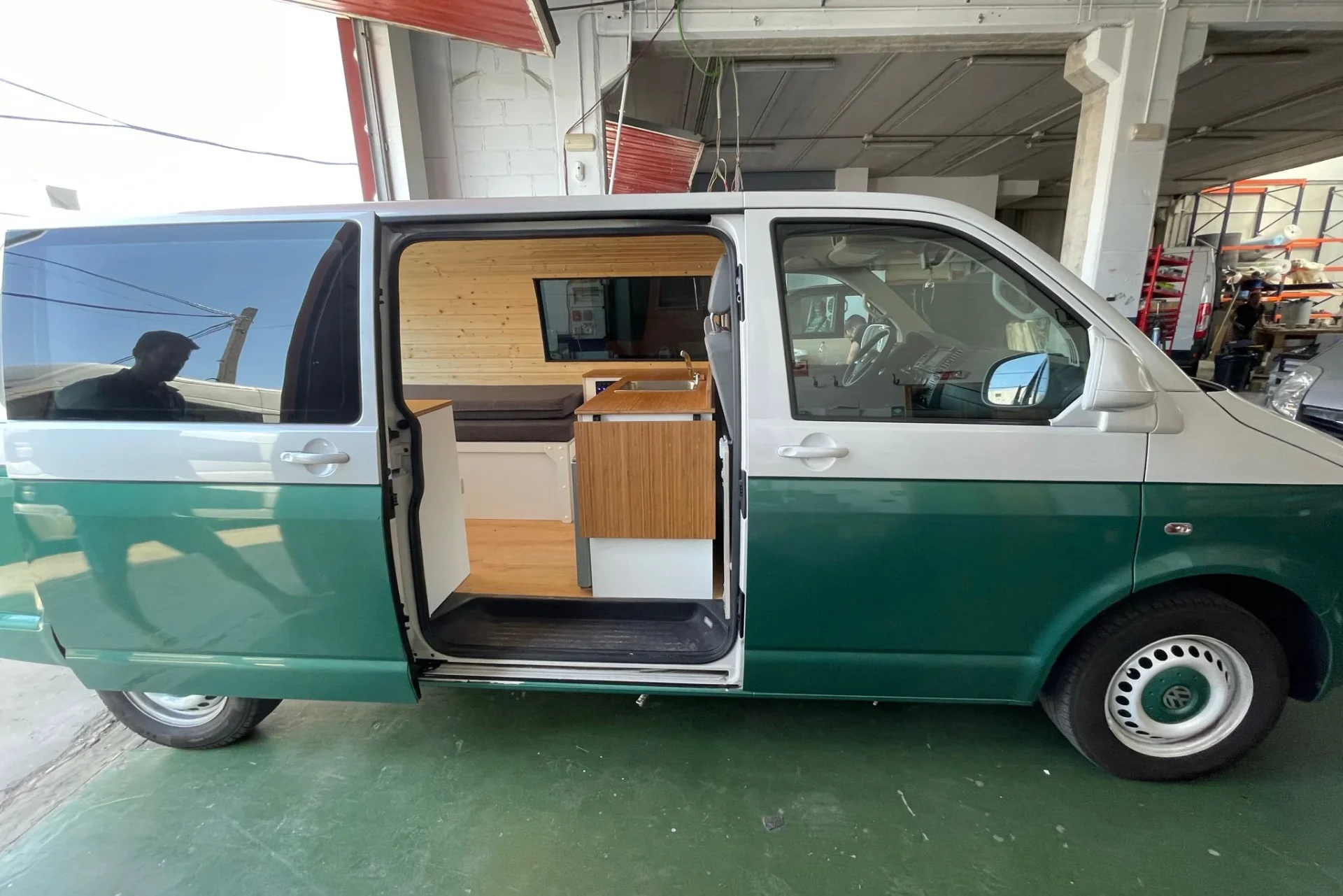 Volkswagen T6 camperizado en tonos verde y blanco, optimizado para 2-3 personas, con la puerta lateral abierta mostrando el interior