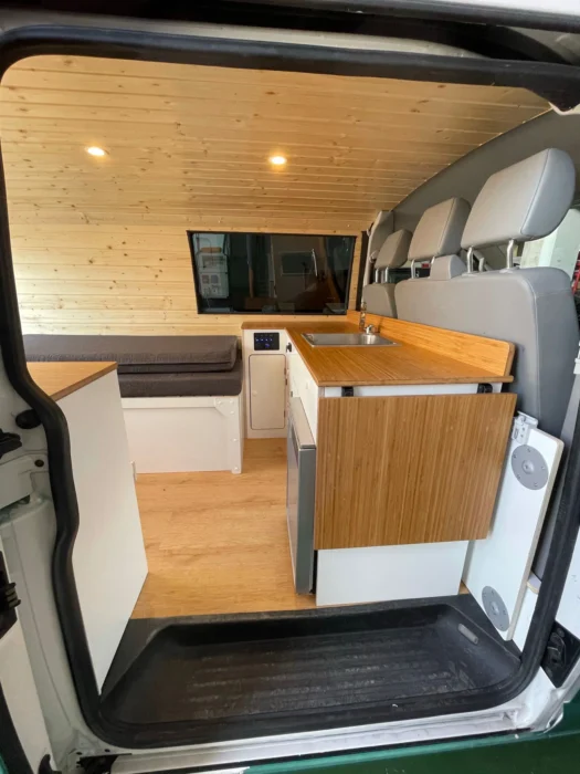 VW T6 Camper con encimera en blanco y madera, amplio espacio de trabajo, techo de madera y ventanas.