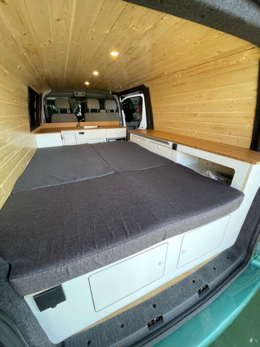 Detalles de la cama de la VW T6 Camper completamente extendida, mostrando su tamaño y que ocupa toda la parte trasera de la furgoneta.