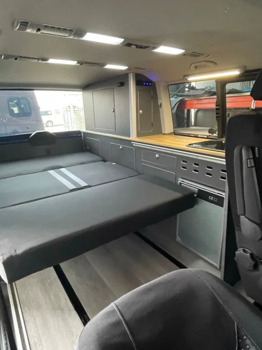 VW T6 Camper con detalle de la cama abierta y cómo se utiliza el espacio de descanso deslizando las sillas hacia delante.