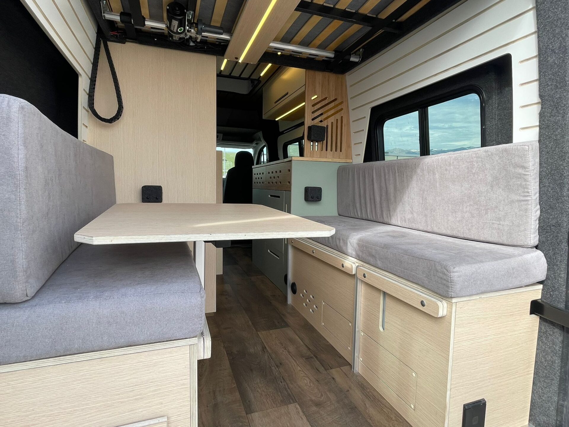Interior del camper Baovan con asientos de tela gris, mesa plegable y almacenamiento lateral, listo para la vida en la carretera.