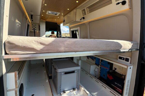 zona trasera de furgoneta camperizada con cama y zona de almacenamiento
